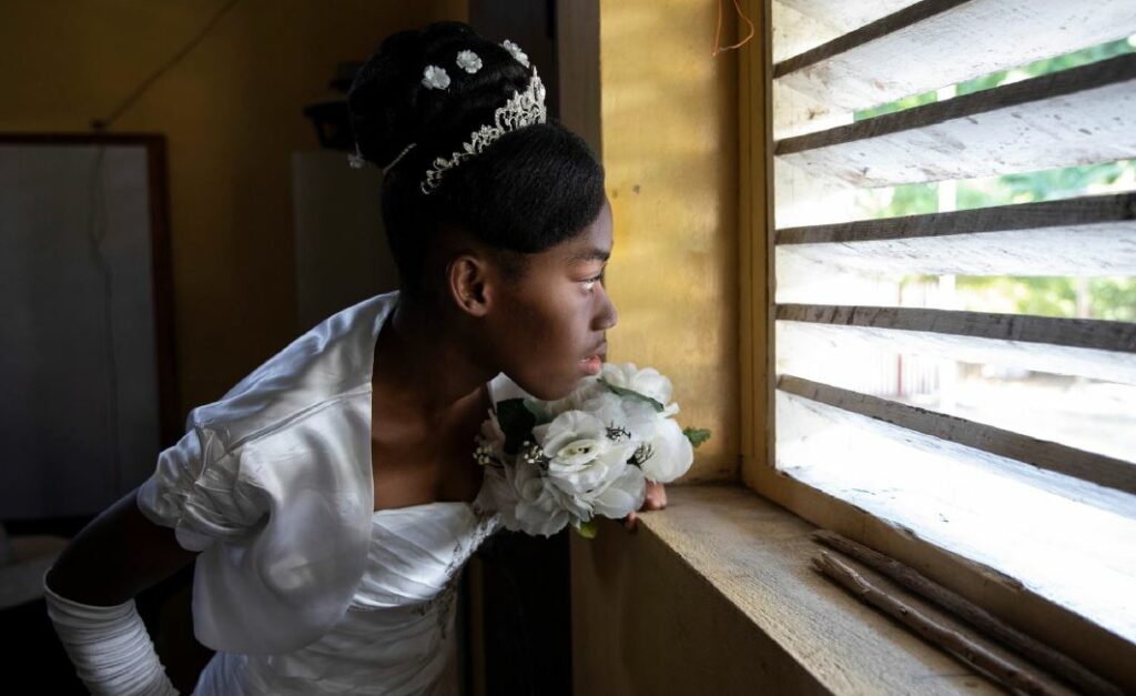 Imagen fotográfica de una adolescente afrodescendiente de Colombia con un vestido de novia, la cual aparentemente se está escondiendo de alguien.