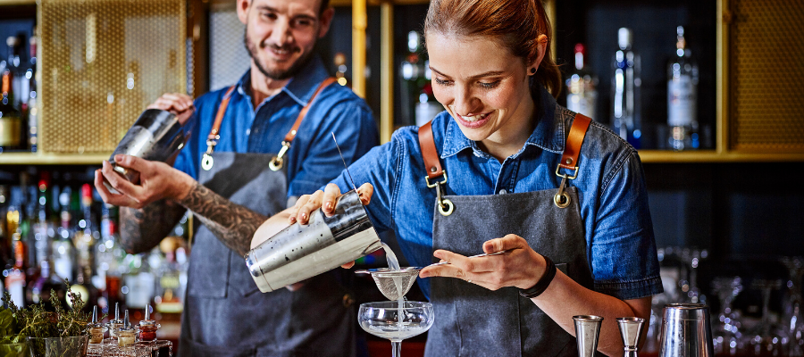 Imagen ilustrativa en la que dos personas (mujer y hombre jóvenes) preparan bebidas de coctelería. Imagen origonal en: https://www.diageobaracademy.com/