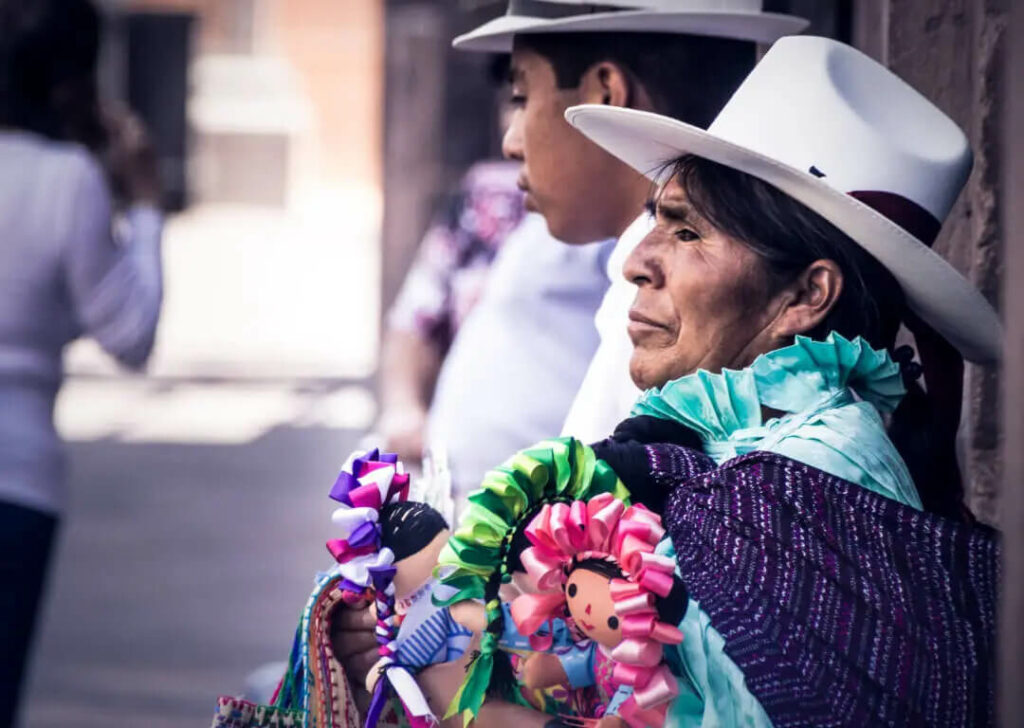 Imagen de mujer indígena, la cual sostiene un par de muñecas con vestidos tradicionales mexicanos. Imagen tomada del estudio Hambre y Género. 