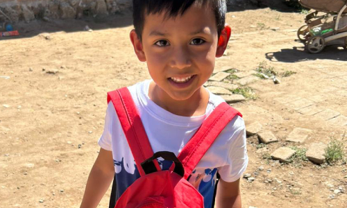 Niño asistente del programa Heinz sabor que inspira, sonriendo a la cámara y cargando una mochila del programa.