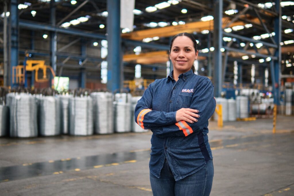 En imagen una mujer sonriendo y de forno una empresa de metales y acero